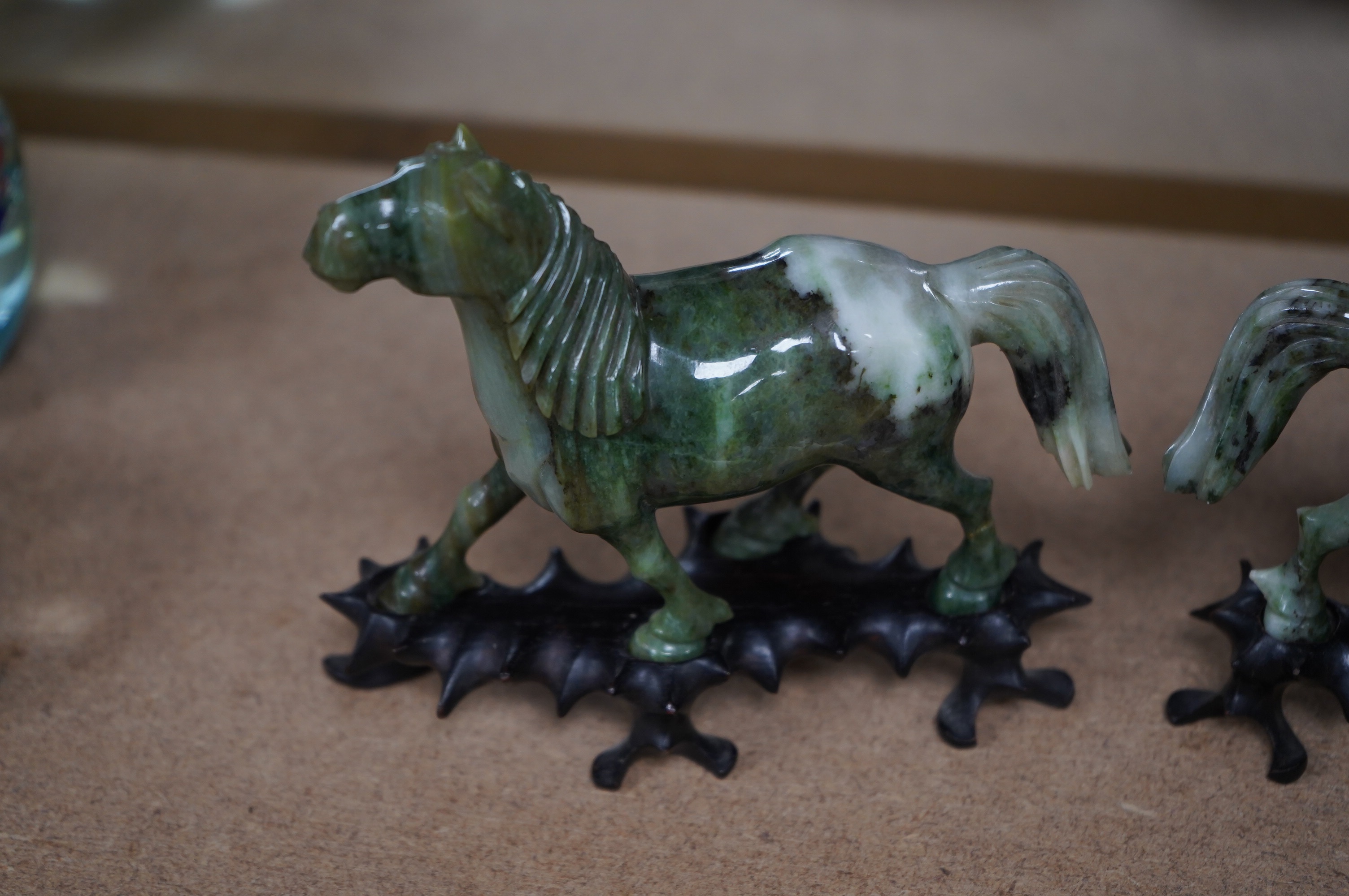 A pair of mid 20th century Chinese jadeite figures of horses, raised on hardwood stands, 13cm wide. Condition - fair, two legs broken and re-glued